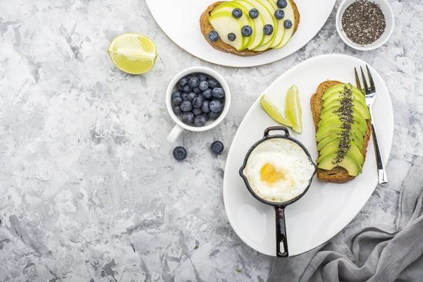 Gezond ontbijt gebakken eieren in een batch koekenpan en toast met groene appel avocado bosbessen op marmeren achtergrond. Kleur jaar. Groen. Bovenaanzicht — Stockfoto