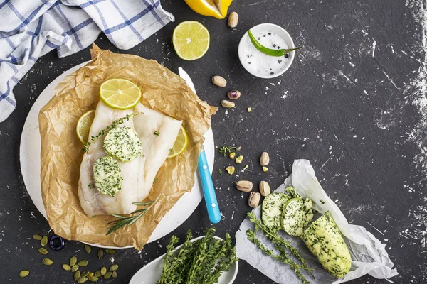 Bacalhau fresco antes de assar com ervas caseiras de manteiga verde em um fundo escuro fatias de limão, tomilho, sal marinho. Vista superior. Conceito de alimentação saudável — Fotografia de Stock