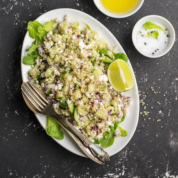 Gesunder Salat zum Mittagessen oder Snack aus Quinoa und frischem Gemüse in einem ovalen weißen Teller auf dunklem Hintergrund. Ansicht von oben. — Stockfoto