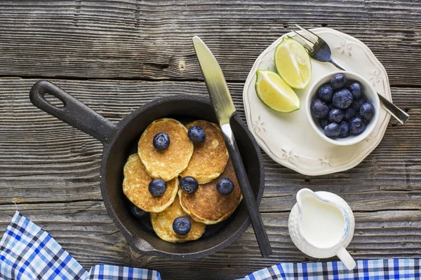 Petit déjeuner d'été sain. Poêle noire en fonte avec crêpes d'avoine fraîches, bleuets et miel liquide sur fond de bois foncé . — Photo