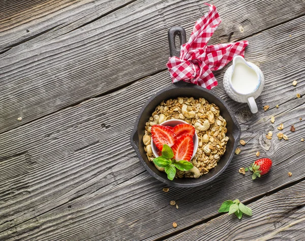 Egészséges reggeli. Otthoni ropogós arany granola friss eper, kesudió és a méz egy öntöttvas serpenyőben, fából készült háttér. Szemközti nézet. — Stock Fotó