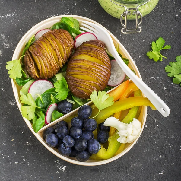 Здоровая закуска в коробке для обеда: картофель с золотой выпечкой, салат, черника, зеленый перец, цветная капуста, редис в пластиковом контейнере с вилкой. Вид сверху — стоковое фото