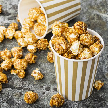 İştah açıcı ev yapımı karamel patlamış mısır şeritli klasik kağıt bardak gri bir arka plan üzerinde. Seçici odak.