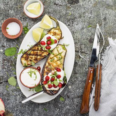 Yarıya patlıcan ekşi krema sosu, otlar, zeytinyağı, sarımsak, gri bir arka plan üzerine nar taneleri ile çatal ile ızgara. Üstten Görünüm.