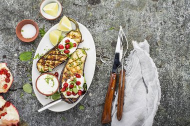 Yarıya patlıcan ekşi krema sosu, otlar, zeytinyağı, sarımsak, gri bir arka plan üzerine nar taneleri ile çatal ile ızgara. Üstten Görünüm.