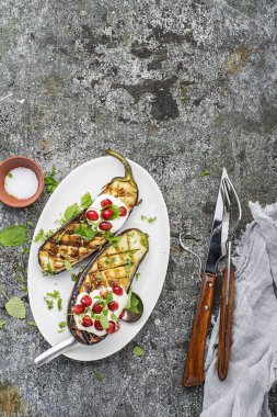 Yarıya patlıcan ekşi krema sosu, otlar, zeytinyağı, sarımsak, gri bir arka plan üzerine nar taneleri ile çatal ile ızgara. Üstten Görünüm.