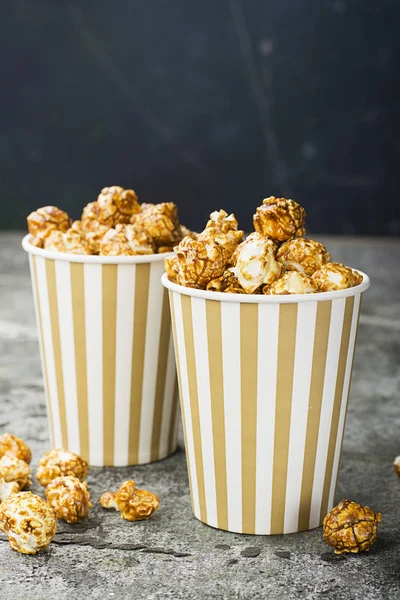 Apetitivas palomitas de caramelo caseras en tazas de papel clásicas a rayas sobre un fondo gris. Enfoque selectivo . —  Fotos de Stock