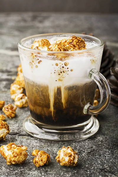 Un verre de café au lait sucré appétissant avec une mousse crémeuse surmontée de pop-corn croustillant au caramel sur un fond de pierre grise. Concentration sélective . — Photo