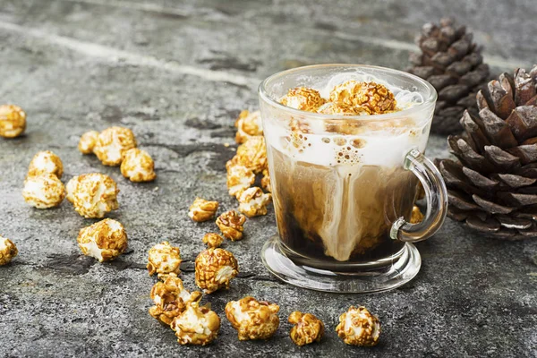Sklenici lahodné sladké mléko kávu s krémovou pěnou přelitý karamel křupavý popcorn na šedém pozadí kamene. Selektivní fokus. — Stock fotografie