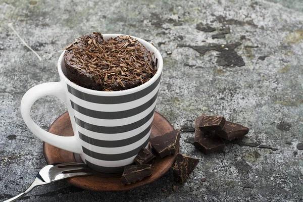 Gâteau de tasse aromatique au chocolat fait maison dans une tasse rayée grise élégante sur un fond de pierre grise avec des morceaux de chocolat amer. Concentration sélective . — Photo