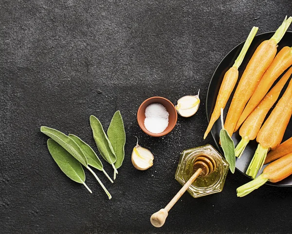 Young juicy carrots, sage, floral honey, garlic, salt ingredients for baking caramel spicy carrots. Top View. — Stock Photo, Image