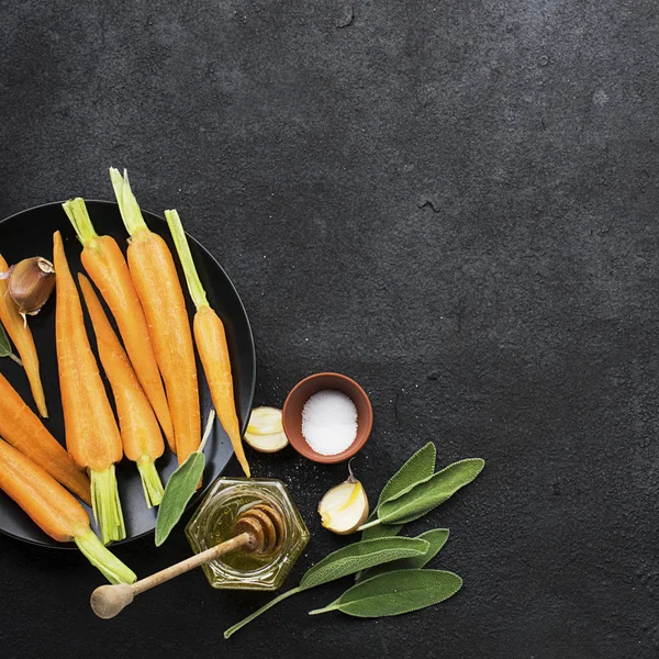 Young juicy carrots, sage, floral honey, garlic, salt ingredients for baking caramel spicy carrots. Top View. — Stock Photo, Image