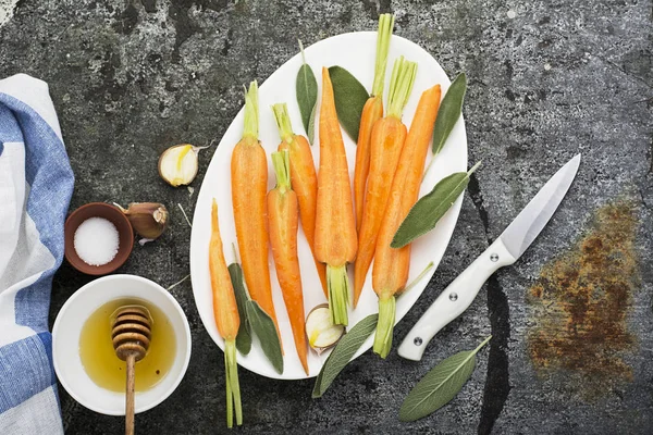 Young juicy carrots baked with honey, sage, garlic, olive oil, salt for a homely comfortable dinner on the background. Top View. — Stock Photo, Image