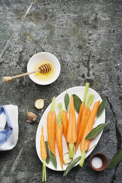 若いジューシーなニンジンは蜂蜜、セージ、ニンニク、オリーブ オイル、塩、背景の家庭的な快適な夕食の焼き。トップ ビュー. — ストック写真