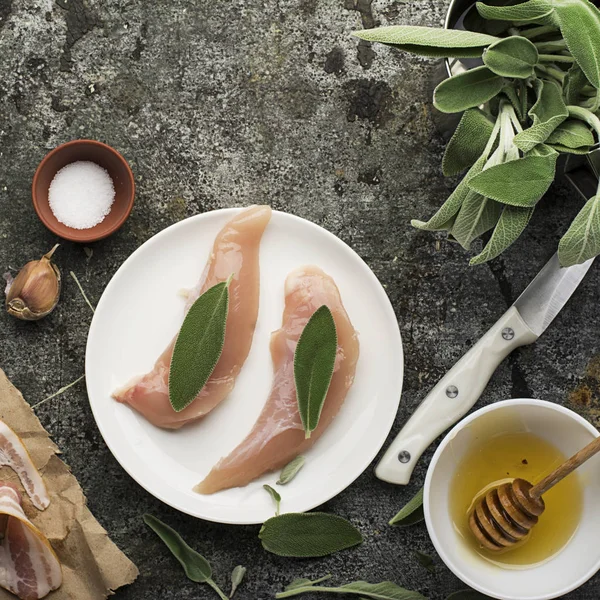 Куриные грудки с листьями шалфея, цветочный мед, соль, оливковое масло, чеснок, с тонкими полосками бекона перед выпечкой. Вид сверху . — стоковое фото