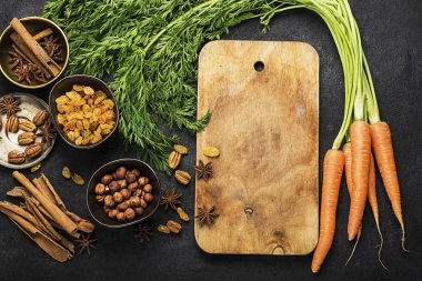 Malzemeler geleneksel klasik havuç için aromalı sonbahar mevsim pasta: sulu taze havuç, Kuru üzüm, baharatlar, baharat, tatlım, karanlık bir arka plan üzerinde fındık. Üstten Görünüm.