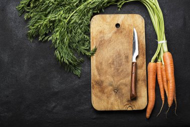 Bir avuç taze sulu havuç bir başında bir vintage kesme tahtası ve akşam yemeği yemek için bir bıçak karanlık bir arka plan ile. Üstten Görünüm.