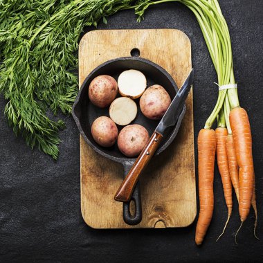 Taze organik tarım sebze: havuç, patates, taze otlar, baharatlar ve karanlık dokulu bir arka plan ile bir vintage kesme tahtası ve bıçak üzerine. Üstten Görünüm.