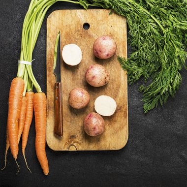 Taze organik tarım sebze: havuç, patates, taze otlar, baharatlar ve karanlık dokulu bir arka plan ile bir vintage kesme tahtası ve bıçak üzerine. Üstten Görünüm.