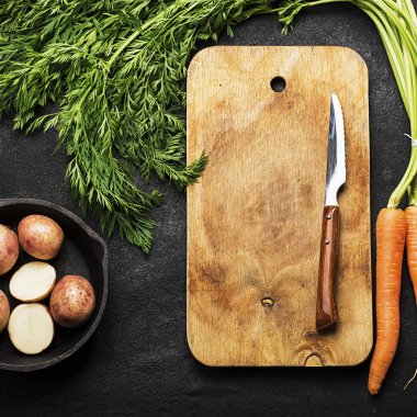 Taze organik tarım sebze: havuç, patates, taze otlar, baharatlar ve karanlık dokulu bir arka plan ile bir vintage kesme tahtası ve bıçak üzerine. Üstten Görünüm.