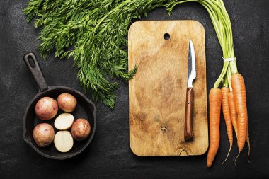 Taze organik tarım sebze: havuç, patates, taze otlar, baharatlar ve karanlık dokulu bir arka plan ile bir vintage kesme tahtası ve bıçak üzerine. Üstten Görünüm.