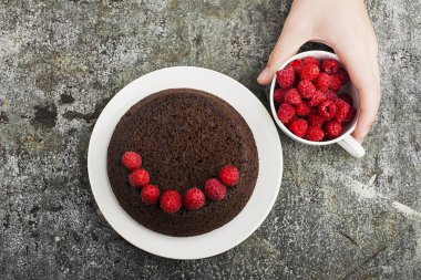 Çılgın ev yapımı kek çikolata ahududu ile gri bir arka plan üzerinde erkek eller tarafından dekore edilmiş. Üstten Görünüm.