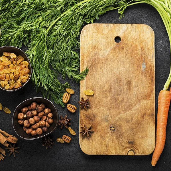 Ingredients for the traditional classic carrot flavored autumn seasonal pie: juicy fresh carrots, raisins, spices, spices, honey, nuts on a dark background. Top View. — Stock Photo, Image