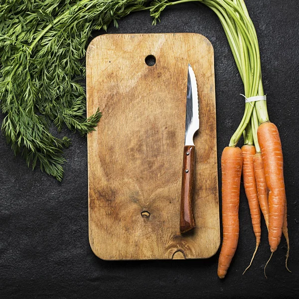 Bir avuç taze sulu havuç bir başında bir vintage kesme tahtası ve akşam yemeği yemek için bir bıçak karanlık bir arka plan ile. Üstten Görünüm.