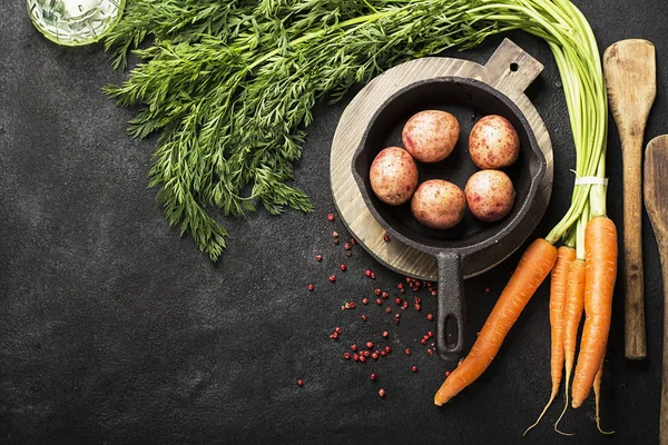 Fresh organic farm vegetables: carrots, potatoes, fresh herbs, spices and oil on a dark textured background with a vintage cutting board and knife. Top View. — Stock Photo, Image