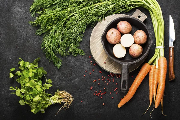 Hortalizas de granja orgánicas frescas: zanahorias, patatas, hierbas frescas, especias y aceite sobre un fondo de textura oscura con una tabla de cortar vintage y un cuchillo. Vista superior . — Foto de Stock