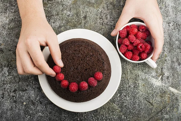 Çılgın ev yapımı kek çikolata ahududu ile gri bir arka plan üzerinde erkek eller tarafından dekore edilmiş. Üstten Görünüm.