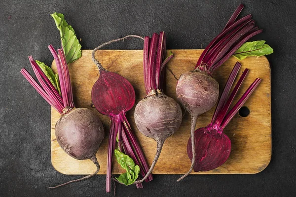 Düz siyah arka plan üzerinde bir vintage ahşap kesme tahtası üzerinde ham organik tarım pancar. Üstten Görünüm.