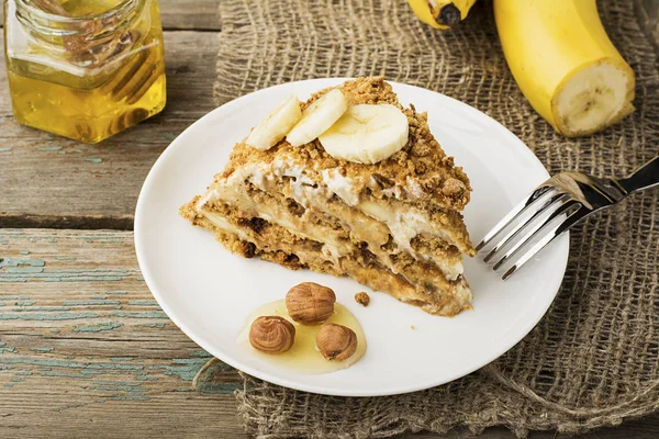 新鮮な自家製バナナ パフ ケーキ ビスケット、サワー クリーム、バナナ スライス、水平デザインのプレーン灰色木製の背景の上に蜂蜜。バック グラウンドでバナナの束. — ストック写真