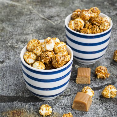 İki seramik beyaz çizgili mavi kase şık gri taş zemin üzerine tatlı karamelli patlamış mısır. Seçici odak.