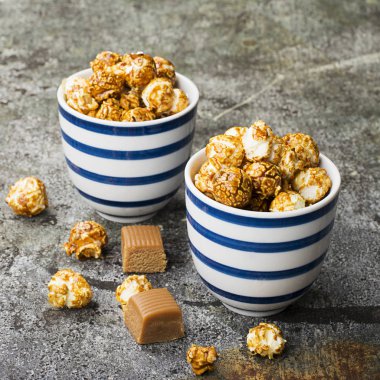 İki seramik beyaz çizgili mavi kase şık gri taş zemin üzerine tatlı karamelli patlamış mısır. Seçici odak.