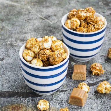 İki seramik beyaz çizgili mavi kase şık gri taş zemin üzerine tatlı karamelli patlamış mısır. Seçici odak.