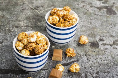 İki seramik beyaz çizgili mavi kase şık gri taş zemin üzerine tatlı karamelli patlamış mısır. Seçici odak.