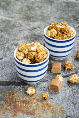 İki seramik beyaz çizgili mavi kase şık gri taş zemin üzerine tatlı karamelli patlamış mısır. Seçici odak.