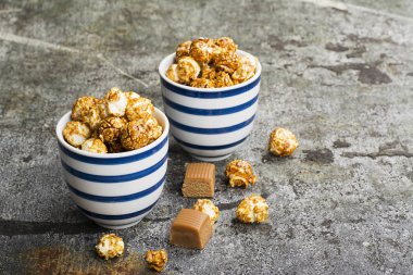 İki seramik beyaz çizgili mavi kase şık gri taş zemin üzerine tatlı karamelli patlamış mısır. Seçici odak.