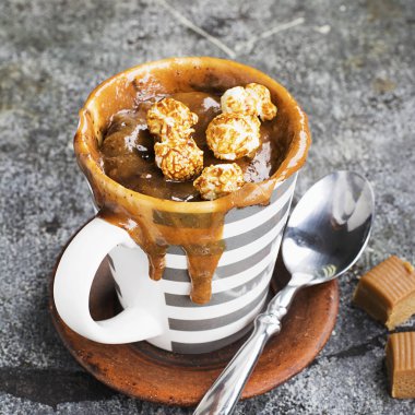 Kupa çörek çikolata ve tuzlu karamel basit bir gri arka plan üzerine bir gri çizgili seramik kupa ile. Seçici odak. Mikrodalga beş dakikalığına snack.