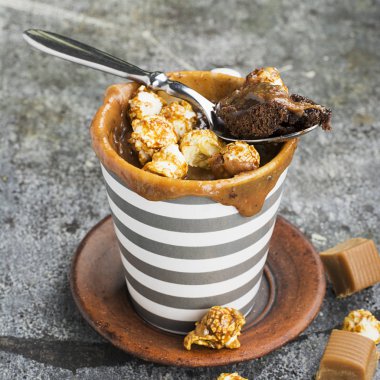 Kupa çörek çikolata ve tuzlu karamel basit bir gri arka plan üzerine bir gri çizgili seramik kupa ile. Seçici odak. Mikrodalga beş dakikalığına snack.