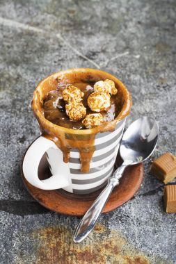 Kupa çörek çikolata ve tuzlu karamel basit bir gri arka plan üzerine bir gri çizgili seramik kupa ile. Seçici odak. Mikrodalga beş dakikalığına snack.