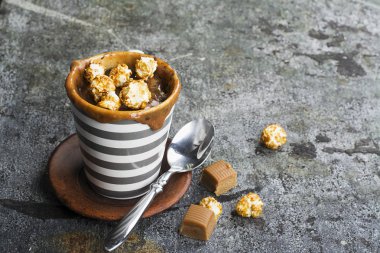 Kupa çörek çikolata ve tuzlu karamel basit bir gri arka plan üzerine bir gri çizgili seramik kupa ile. Seçici odak. Mikrodalga beş dakikalığına snack.