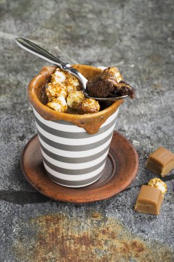 Kupa çörek çikolata ve tuzlu karamel basit bir gri arka plan üzerine bir gri çizgili seramik kupa ile. Seçici odak. Mikrodalga beş dakikalığına snack.