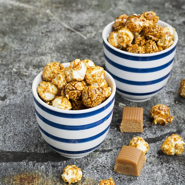 İki seramik beyaz çizgili mavi kase şık gri taş zemin üzerine tatlı karamelli patlamış mısır. Seçici odak.