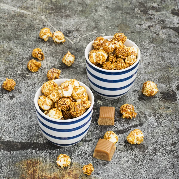 Palomitas dulces de caramelo en dos tazones azules a rayas blancas de cerámica sobre un elegante fondo de piedra gris. Enfoque selectivo . —  Fotos de Stock