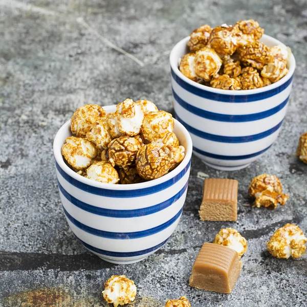 İki seramik beyaz çizgili mavi kase şık gri taş zemin üzerine tatlı karamelli patlamış mısır. Seçici odak.