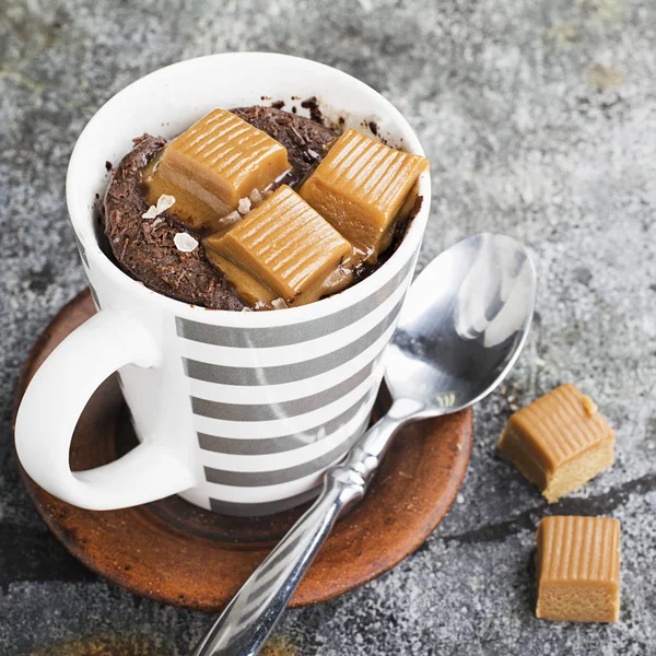 Kupa çörek çikolata ve tuzlu karamel basit bir gri arka plan üzerine bir gri çizgili seramik kupa ile. Seçici odak. Mikrodalga beş dakikalığına snack. — Stok fotoğraf
