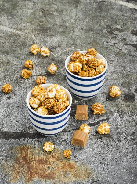 Palomitas dulces de caramelo en dos tazones azules a rayas blancas de cerámica sobre un elegante fondo de piedra gris. Enfoque selectivo . —  Fotos de Stock