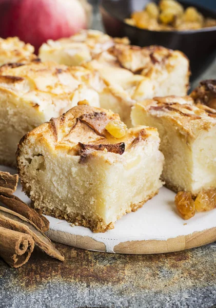 A simple homemade pie with apples and sour cream on a gray background with cinnamon sticks, an apple, caramel sweets. Top view. Selective focus. — Stock Photo, Image